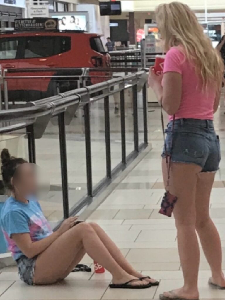 Two women are sitting on the ground in a mall.