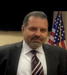 A man in suit and tie standing next to an american flag.